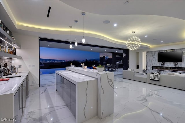 kitchen featuring a raised ceiling, light stone countertops, hanging light fixtures, and a large island