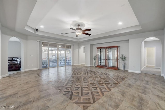 unfurnished living room featuring a raised ceiling and ceiling fan