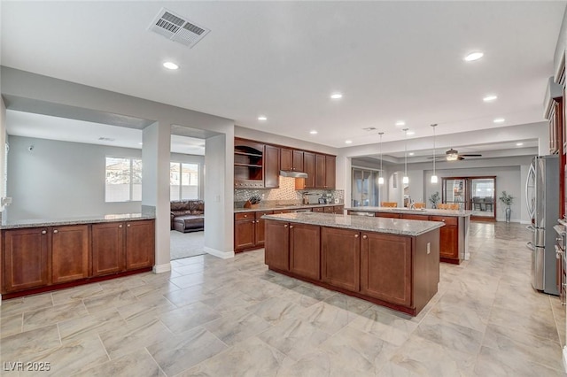 kitchen with ceiling fan, a center island, pendant lighting, stainless steel fridge, and light stone counters