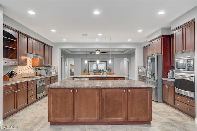 kitchen featuring kitchen peninsula, ceiling fan, stainless steel appliances, decorative light fixtures, and light stone countertops