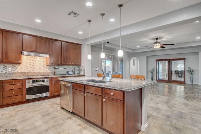 kitchen with an island with sink, ceiling fan, stainless steel appliances, decorative light fixtures, and sink