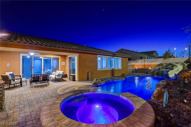 pool at night featuring an in ground hot tub, pool water feature, and a patio