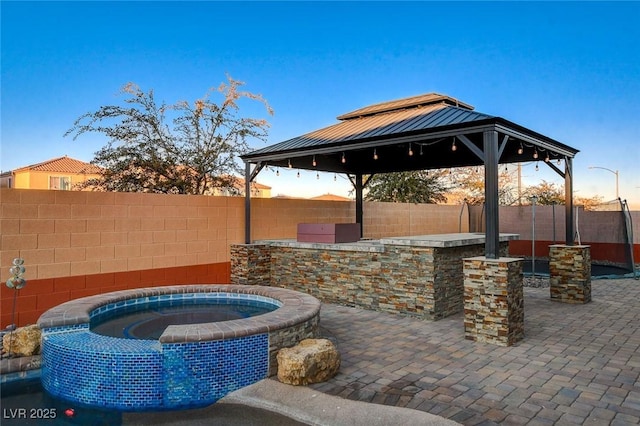 patio terrace at dusk with an in ground hot tub, a gazebo, and a bar