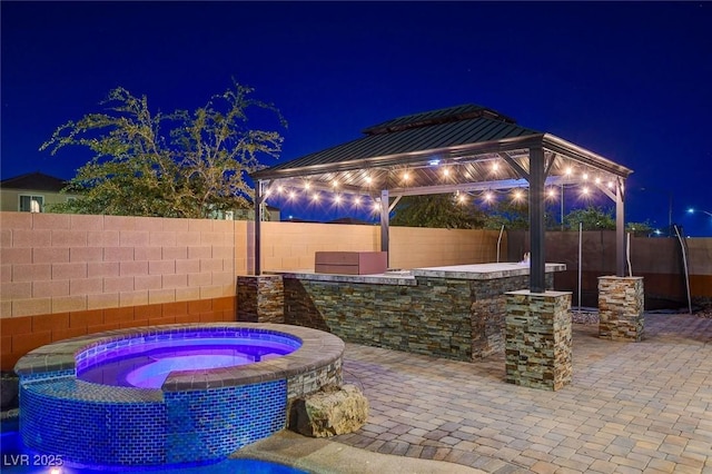 patio at night featuring a gazebo and an in ground hot tub