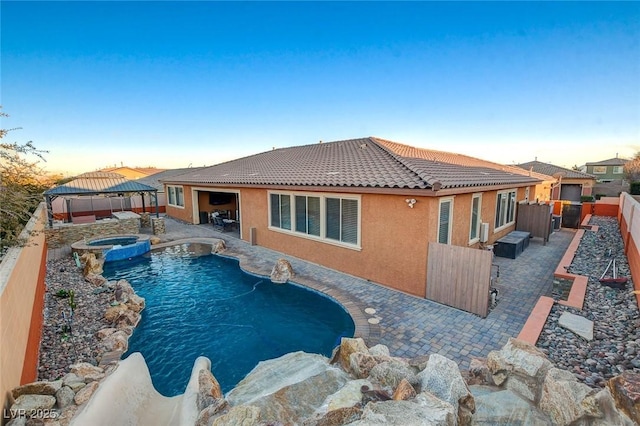 pool at dusk with an in ground hot tub, a gazebo, and a patio