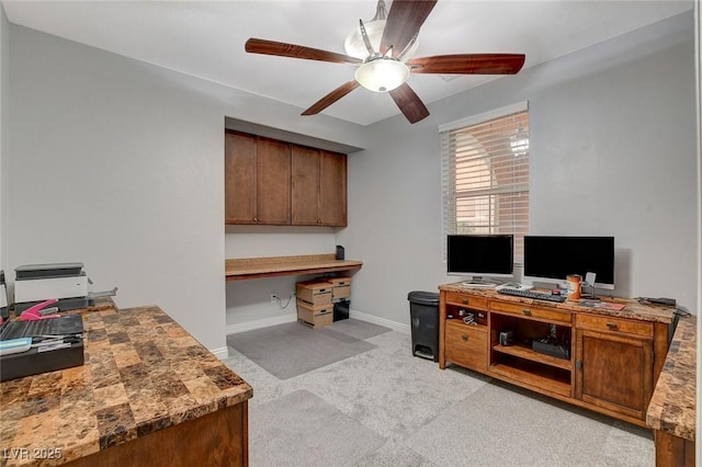 home office with ceiling fan, built in desk, and light colored carpet