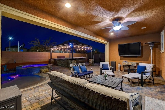 patio at night with an outdoor hangout area, ceiling fan, a gazebo, and an in ground hot tub