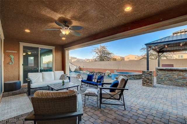 patio terrace at dusk featuring an in ground hot tub, a gazebo, outdoor lounge area, an outdoor bar, and ceiling fan