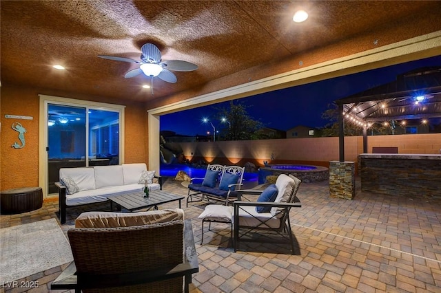 patio at night featuring ceiling fan, an outdoor living space, and a hot tub