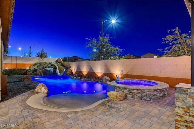 pool at night with pool water feature, a patio, and an in ground hot tub