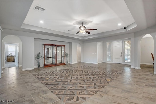 unfurnished living room featuring ceiling fan and a raised ceiling