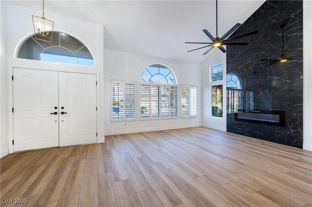 entryway with light wood-type flooring, a high end fireplace, ceiling fan with notable chandelier, and high vaulted ceiling