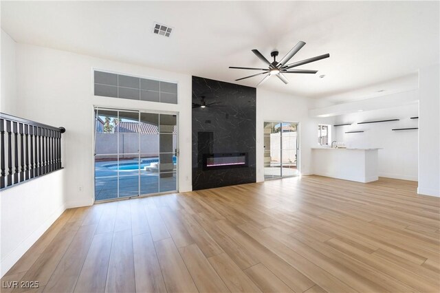 unfurnished living room with ceiling fan, light wood-type flooring, and a fireplace