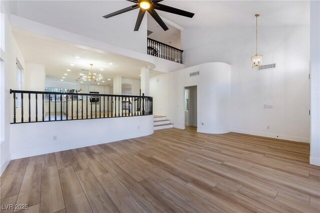 spare room with ceiling fan with notable chandelier, light hardwood / wood-style floors, and a towering ceiling