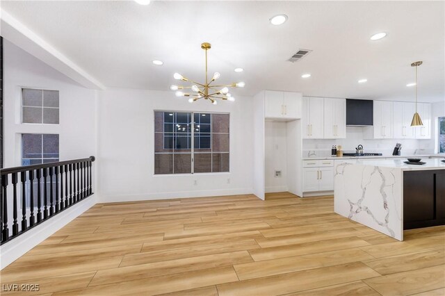 kitchen featuring light stone counters, white cabinets, hanging light fixtures, and a notable chandelier