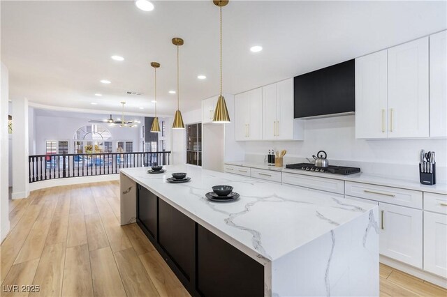 kitchen with light stone countertops, pendant lighting, light hardwood / wood-style flooring, white cabinetry, and stainless steel gas stovetop