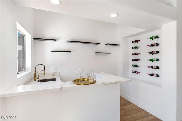 interior space featuring light stone counters, sink, kitchen peninsula, and light wood-type flooring