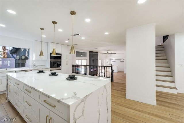 kitchen with light hardwood / wood-style floors, ceiling fan, decorative light fixtures, a kitchen island, and white cabinets