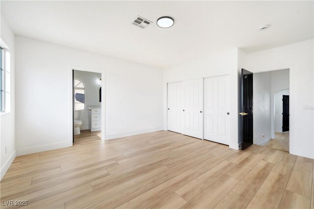 unfurnished bedroom featuring ensuite bath, a closet, and light hardwood / wood-style floors