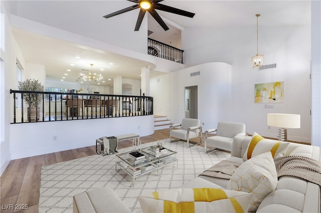 unfurnished living room featuring light hardwood / wood-style floors, ceiling fan with notable chandelier, and a towering ceiling