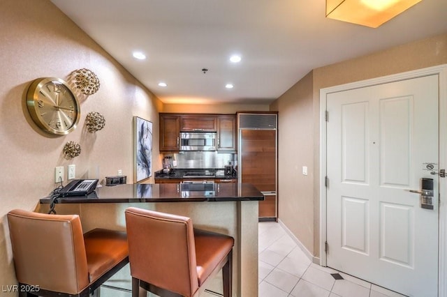 kitchen with light tile patterned floors, a kitchen bar, kitchen peninsula, and paneled fridge