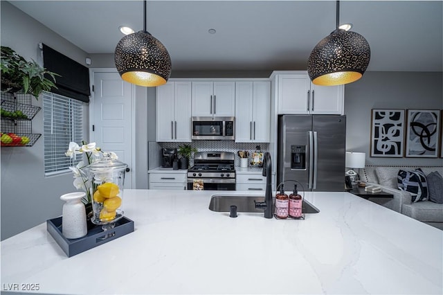 kitchen with hanging light fixtures, white cabinets, backsplash, and stainless steel appliances