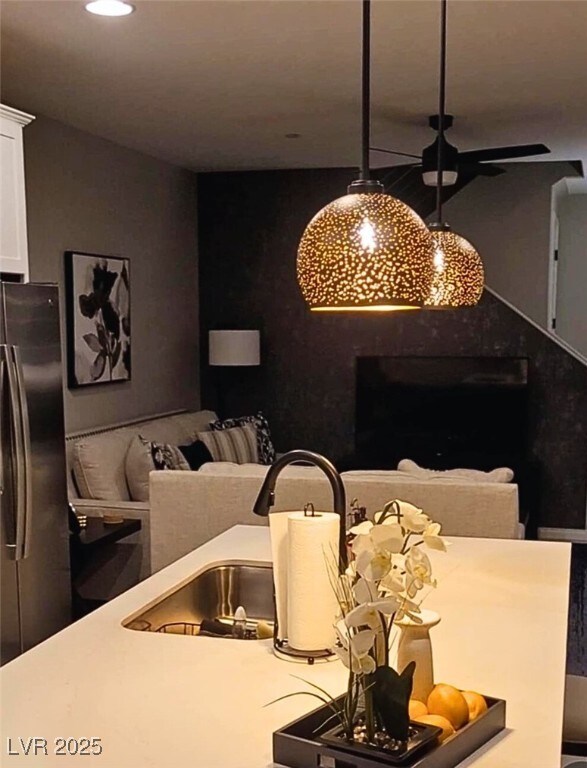 kitchen with stainless steel fridge, ceiling fan, hanging light fixtures, white cabinets, and sink