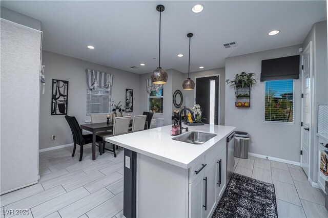 kitchen featuring decorative light fixtures, dishwasher, sink, an island with sink, and white cabinets