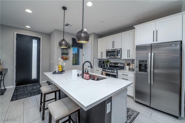 kitchen with decorative light fixtures, sink, appliances with stainless steel finishes, an island with sink, and white cabinets