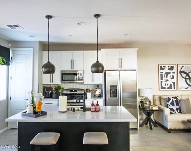 kitchen featuring white cabinetry, pendant lighting, appliances with stainless steel finishes, and a center island with sink