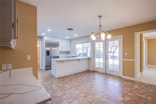 kitchen featuring kitchen peninsula, built in fridge, french doors, pendant lighting, and white cabinets