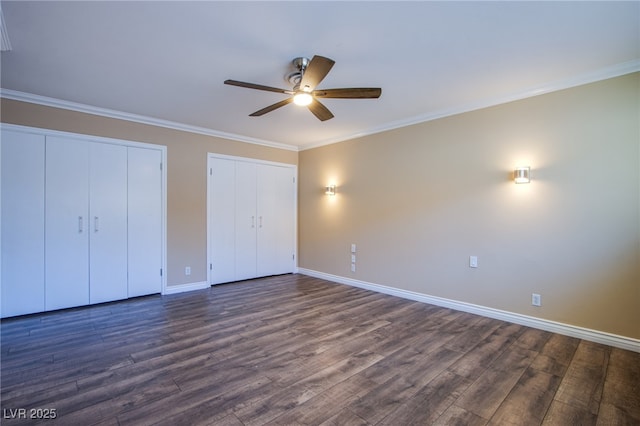 unfurnished bedroom with dark wood-type flooring, ceiling fan, two closets, and crown molding