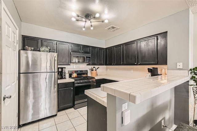 kitchen featuring appliances with stainless steel finishes, backsplash, kitchen peninsula, tile countertops, and light tile patterned floors