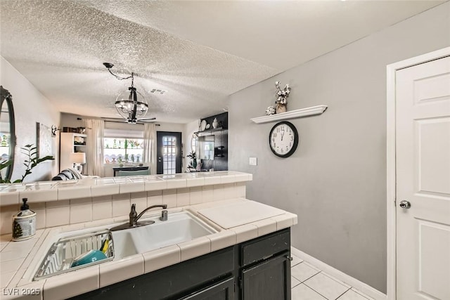 kitchen with light tile patterned floors, ceiling fan, tile counters, hanging light fixtures, and sink