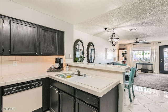 kitchen with tile countertops, kitchen peninsula, ceiling fan, white dishwasher, and pendant lighting