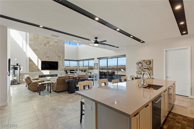 kitchen with a kitchen bar, an island with sink, sink, ceiling fan, and a tiled fireplace