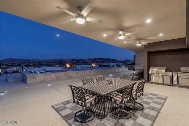 patio at night with ceiling fan, an outdoor kitchen, and a mountain view