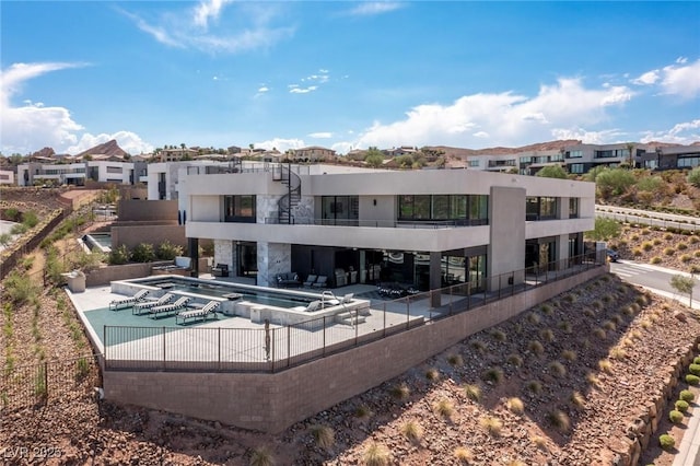 rear view of house featuring a patio, a residential view, a community pool, fence, and stucco siding