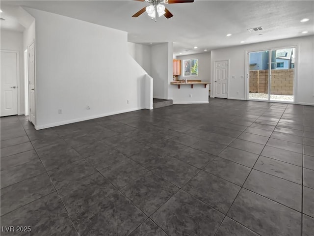 unfurnished living room with ceiling fan, dark tile patterned floors, and a healthy amount of sunlight