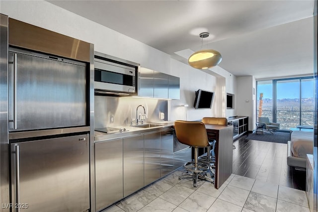 kitchen with appliances with stainless steel finishes, a wall of windows, stainless steel counters, and sink