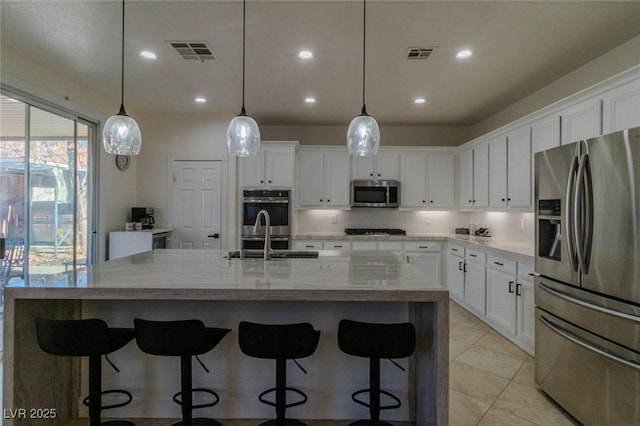 kitchen featuring appliances with stainless steel finishes, a large island with sink, white cabinetry, and decorative light fixtures