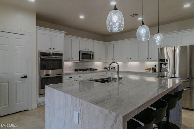 kitchen with appliances with stainless steel finishes, an island with sink, light stone counters, and sink