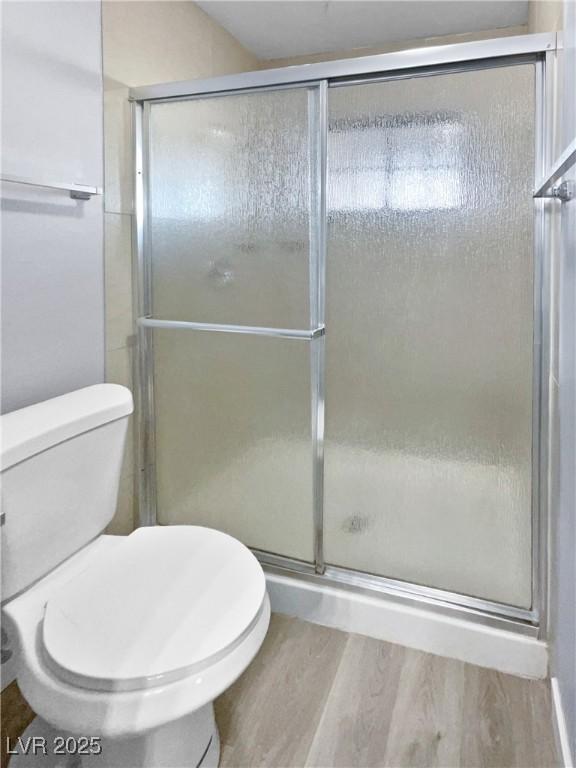 bathroom with wood-type flooring, an enclosed shower, and toilet