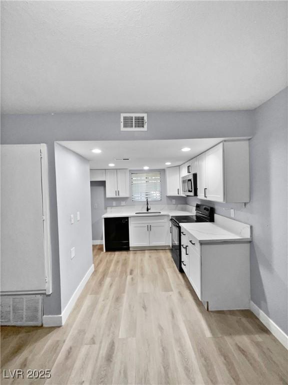 kitchen featuring black appliances, white cabinets, sink, and light hardwood / wood-style flooring