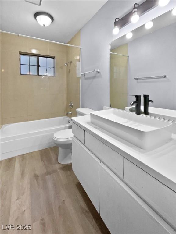 full bathroom with toilet, tiled shower / bath combo, hardwood / wood-style floors, and vanity