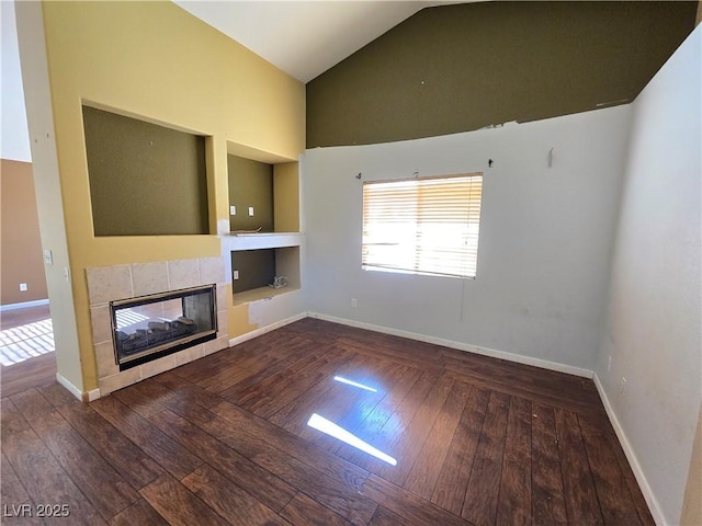 unfurnished living room featuring built in shelves, a tiled fireplace, vaulted ceiling, and dark hardwood / wood-style flooring