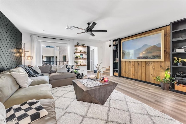 living room with ceiling fan, wooden walls, and light hardwood / wood-style flooring