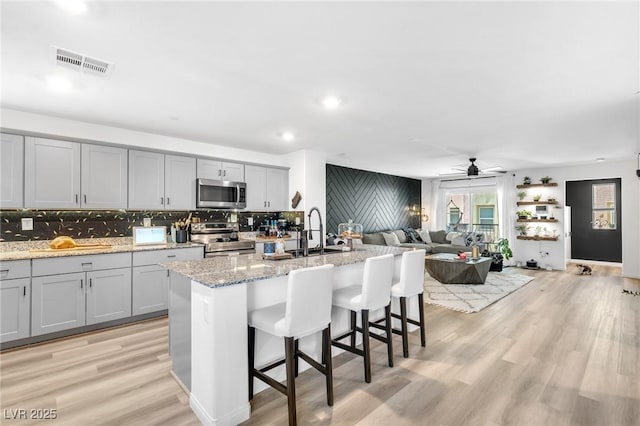 kitchen featuring ceiling fan, light stone countertops, appliances with stainless steel finishes, and a center island with sink