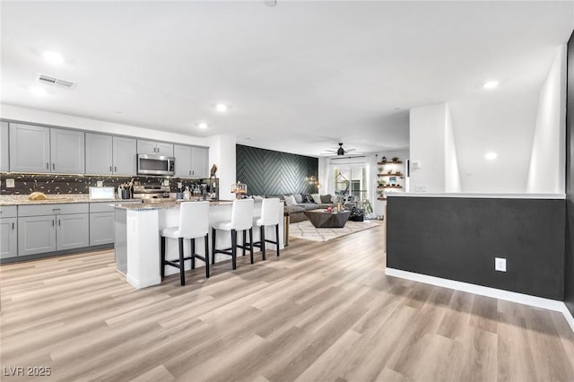 kitchen with ceiling fan, a kitchen bar, gray cabinets, and an island with sink