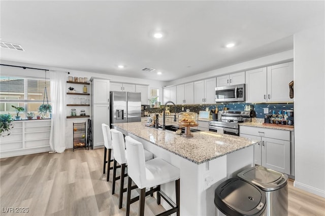 kitchen featuring light stone countertops, a kitchen bar, stainless steel appliances, an island with sink, and sink